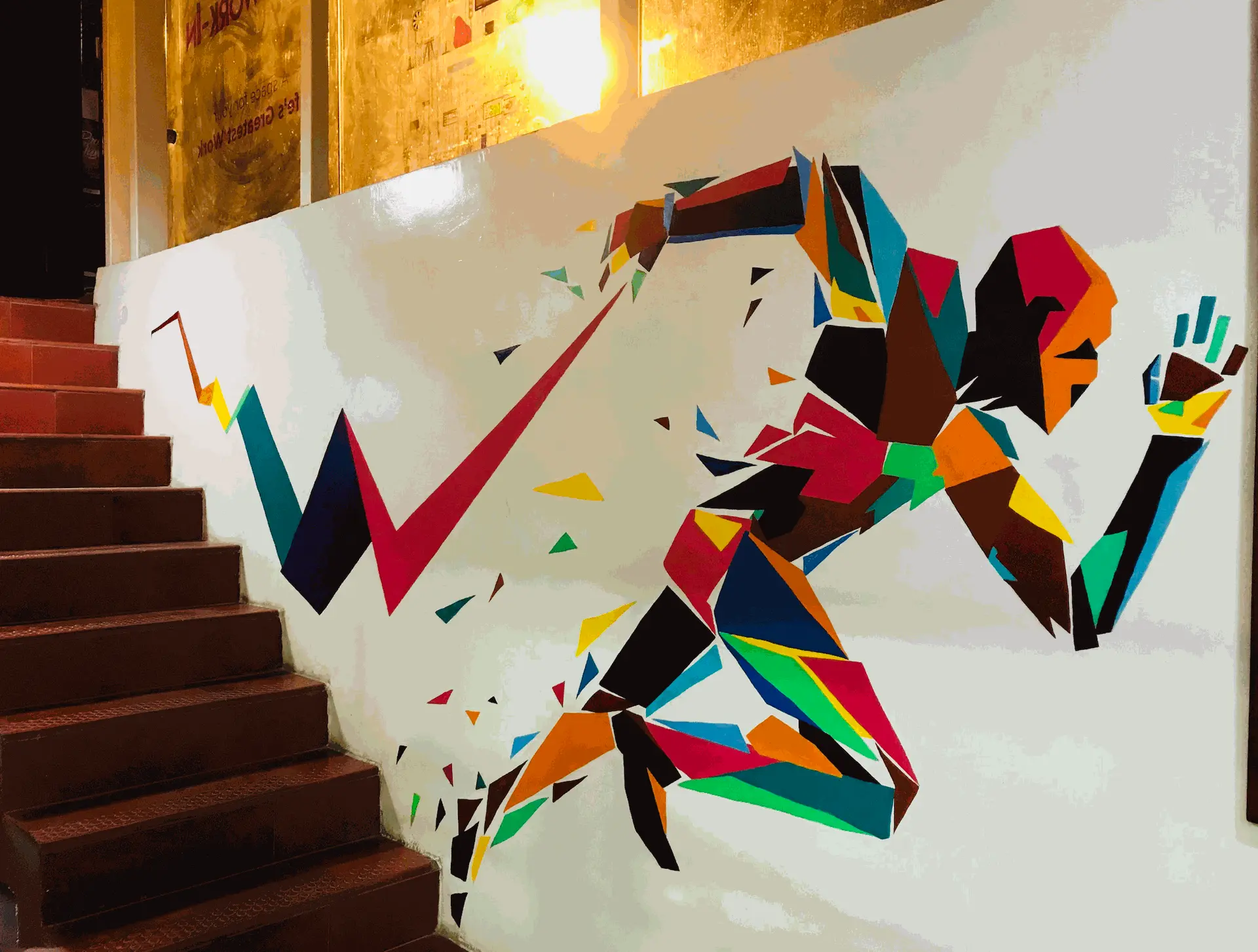 Geometric running man mural on staircase wall at WeWork Bangalore, hand-painted by mounik.art to represent energy and momentum